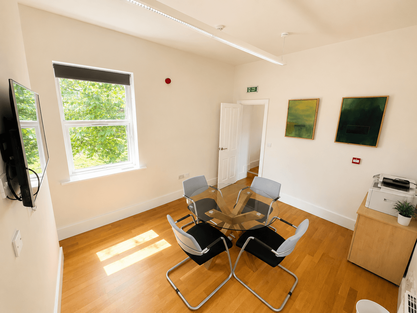 A smaller meeting space at 21 The Grove: round glass table, four chairs and a wall-mounted screen